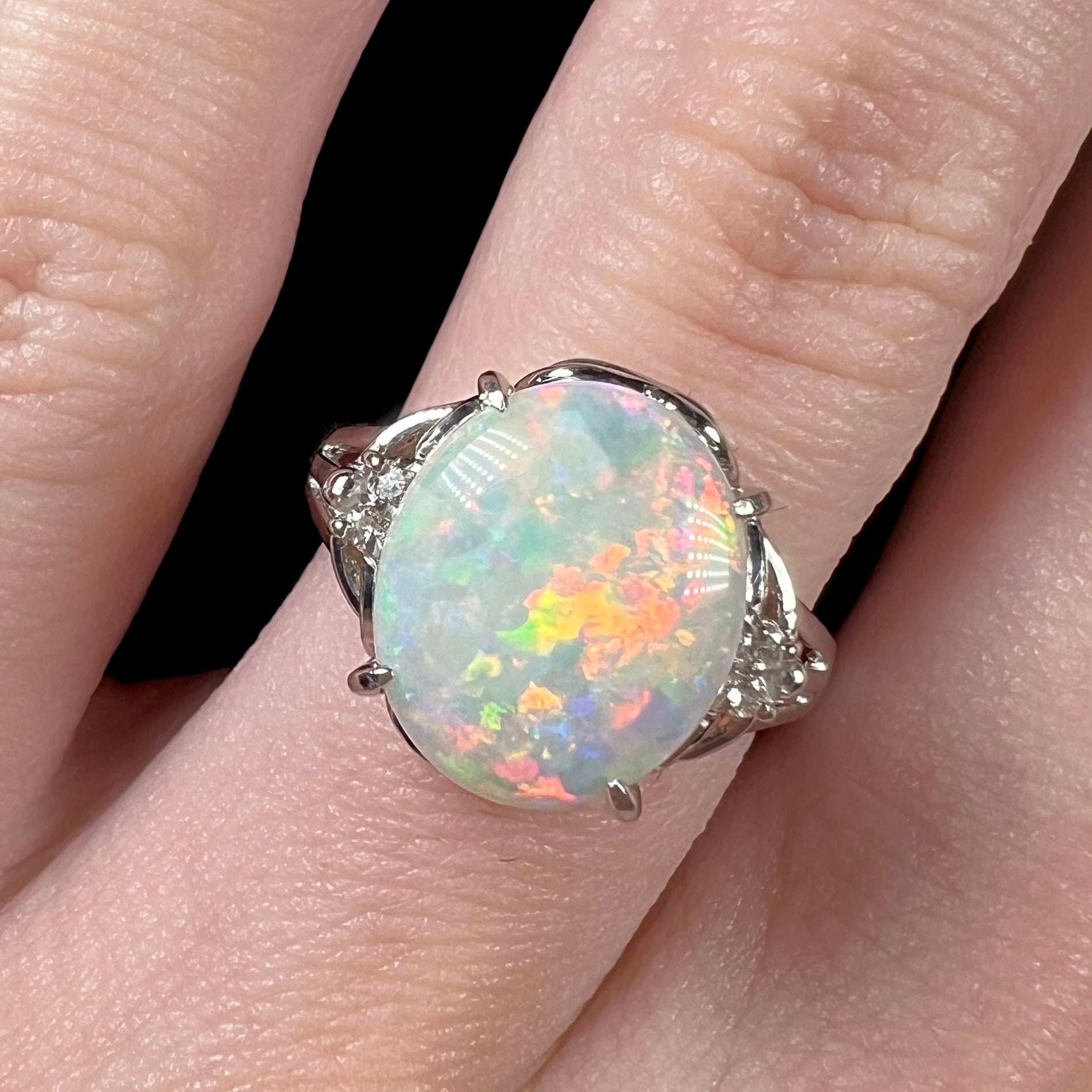 A platinum opal and diamond ring on a finger.  The opal shows red and orange colors.