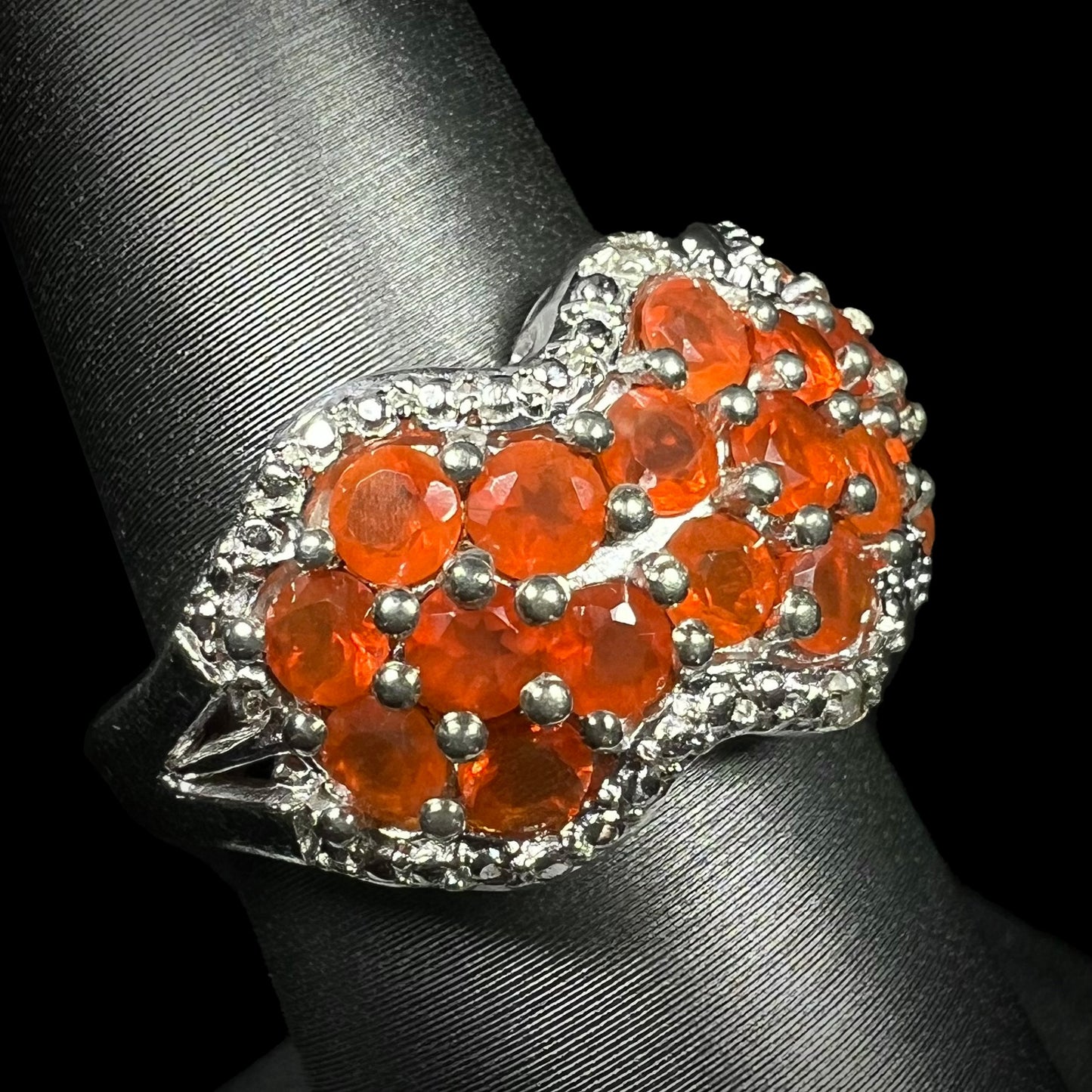 An orange Mexican fire opal sterling silver ring with filigree details, shown on a ring display from an angle.