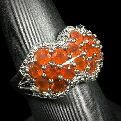 An orange Mexican fire opal sterling silver ring with filigree details, shown on a ring display from an angle.