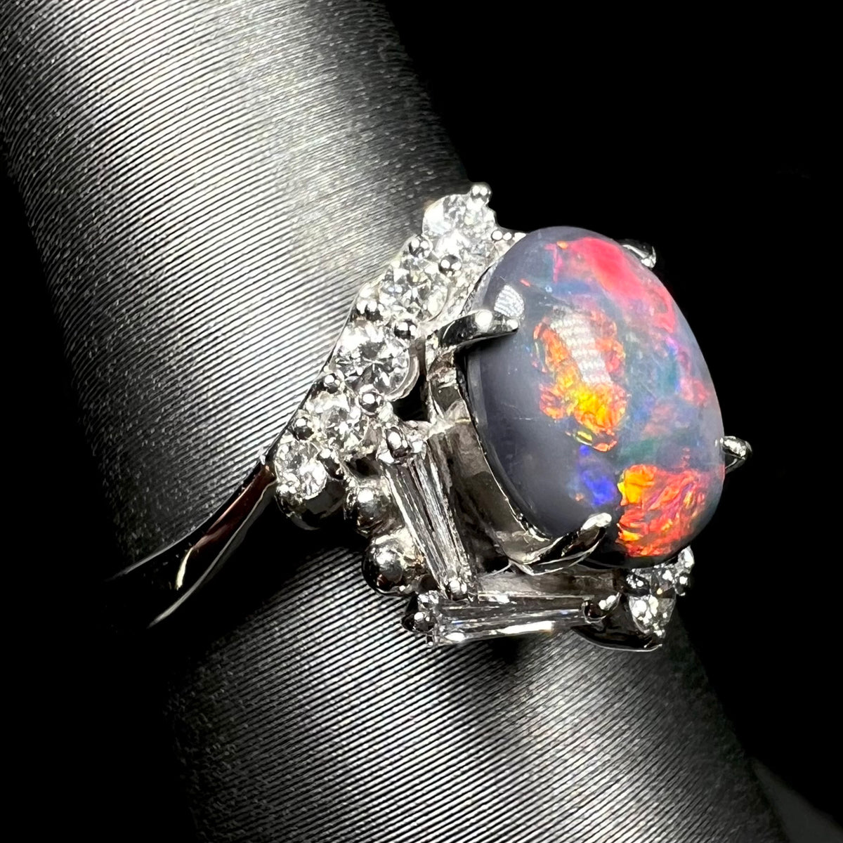 Orange, red, and blue flashes of color seen in Australian dark opal ring, shown from close-up side shoulder view on ring display.