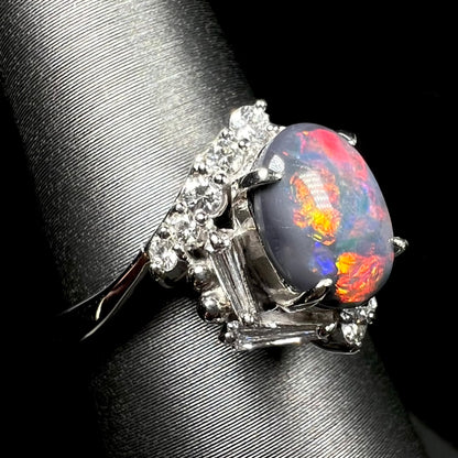 Orange, red, and blue flashes of color seen in Australian dark opal ring, shown from close-up side shoulder view on ring display.