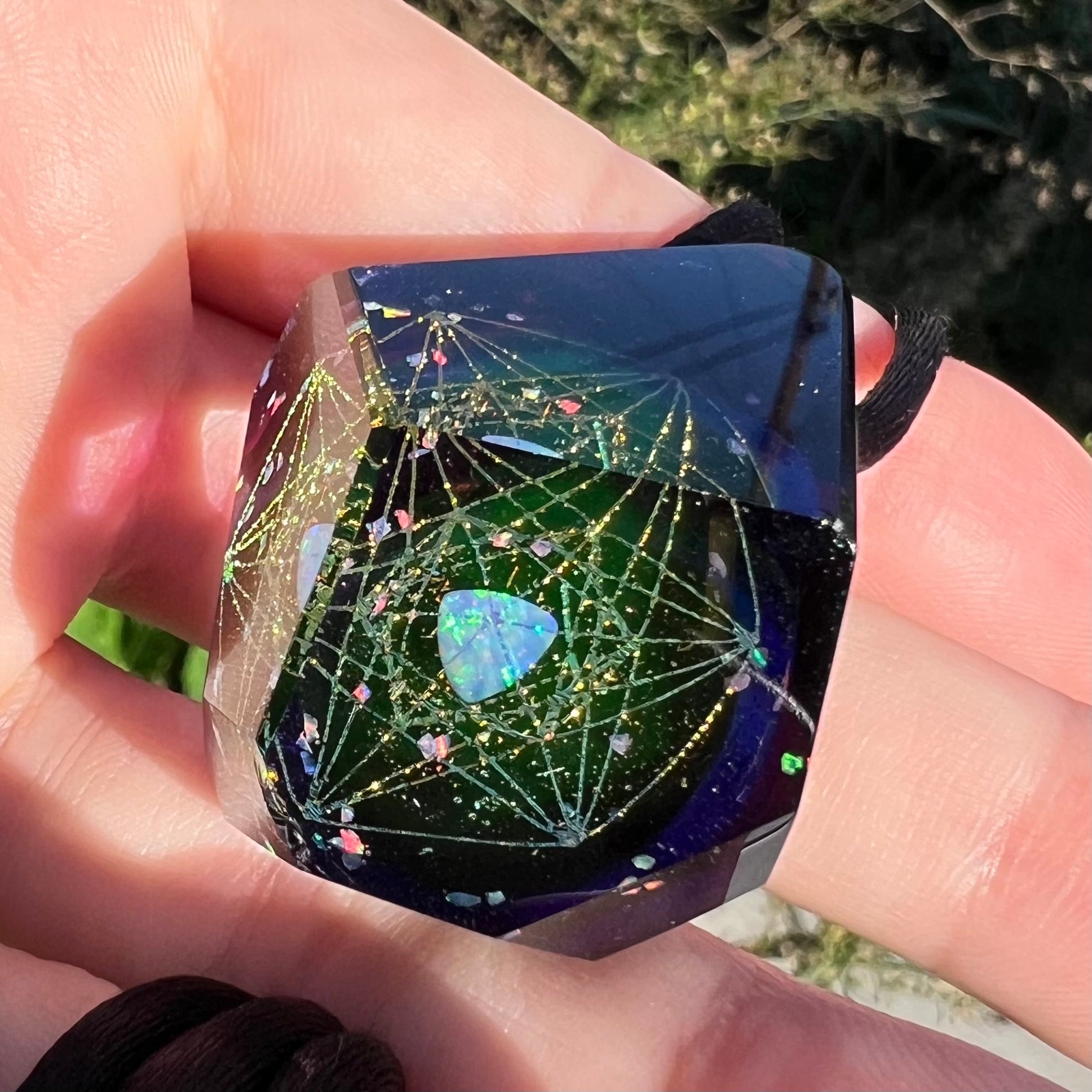 Angled underside close-up of a glass and opal pendant with an outer space motif featuring star designs, shown in the sunlight held in a hand.