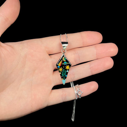 Sterling silver opal and onyx inlay necklace with outer-space motif held in hand against black background.