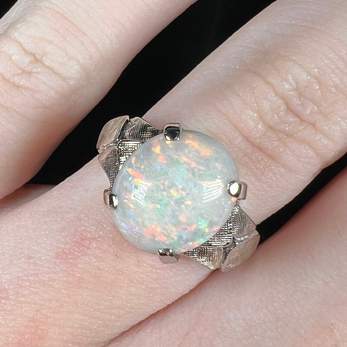 Close-up of an oval-shaped Australian opal solitaire ring in 14k white gold, worn on a finger