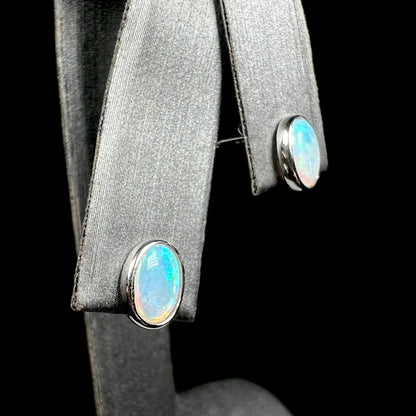 Pair of oval cut Australian crystal opal stud earrings shown close-up on earring display from angled view.