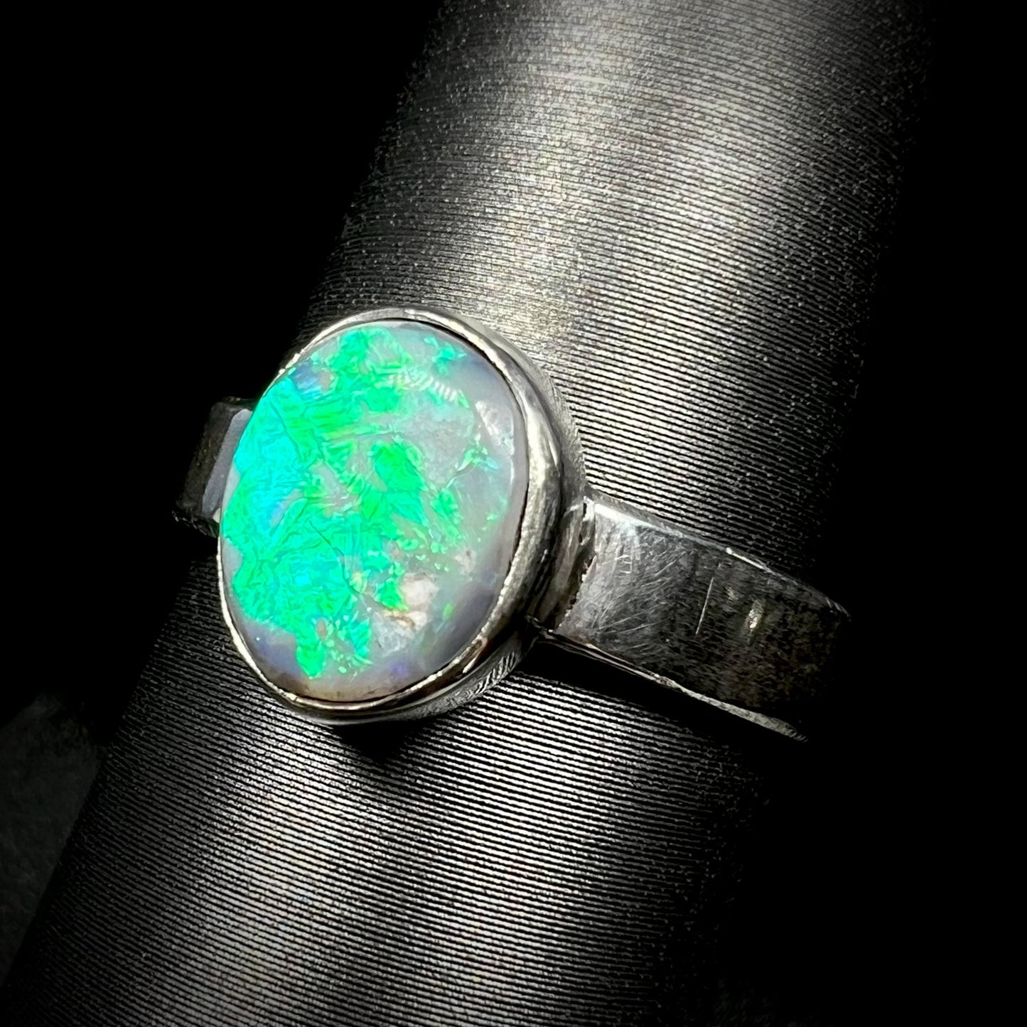 Angled close-up of an oval cut Australian opal ring with a blue and green flash made from sterling silver, shown on a ring display.