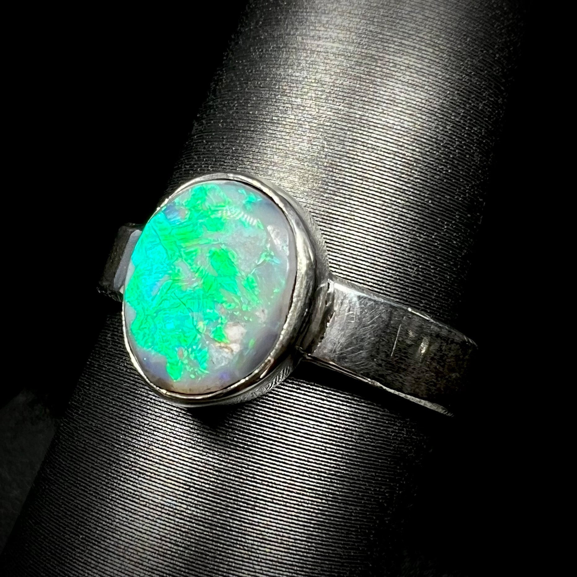 Angled close-up of an oval cut Australian opal ring with a blue and green flash made from sterling silver, shown on a ring display.