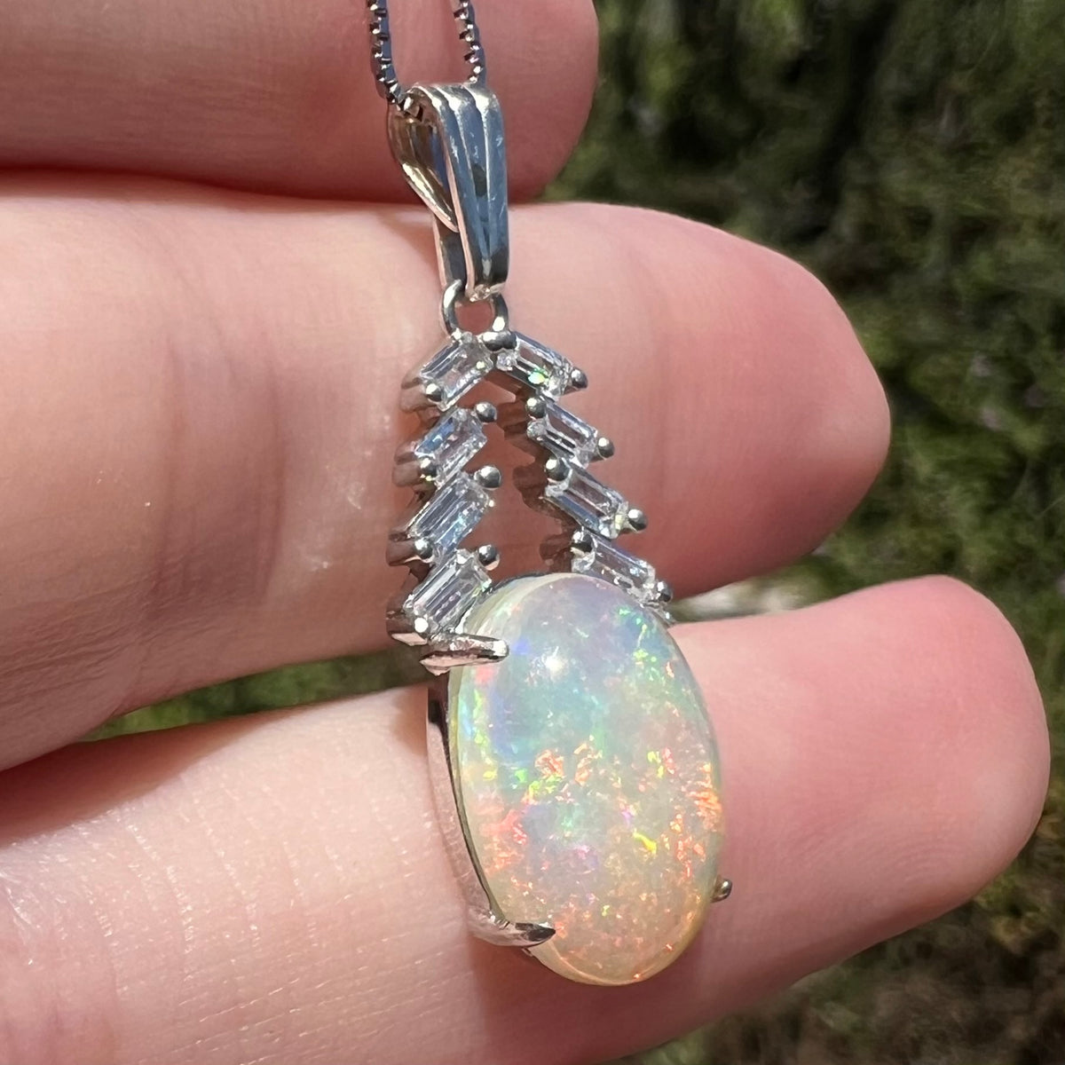 Oval cut Ethiopian opal and CZ pendant in silver, held in hand under natural light