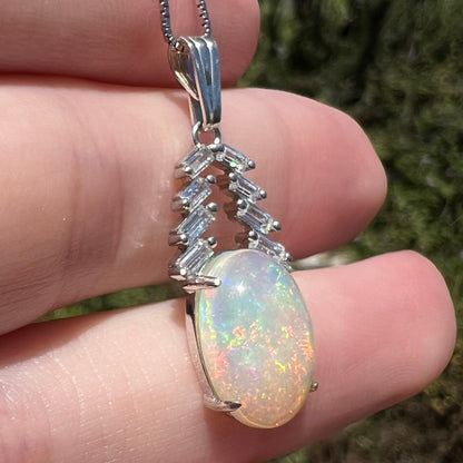 Oval cut Ethiopian opal and CZ pendant in silver, held in hand under natural light