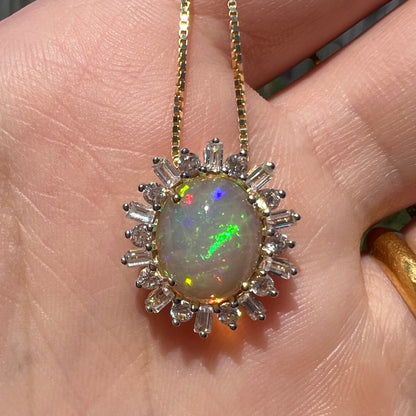 Close-up of oval cut fire opal pendant with spiked halo design held in hand under natural light.  The opal has a green flash.