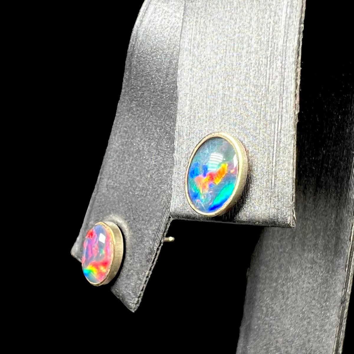 Angled close-up of oval shaped opal triplet stud earrings in gold on earring display