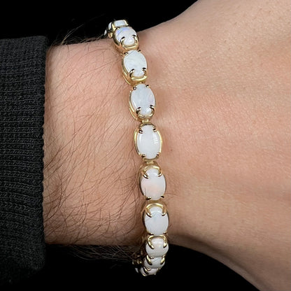 Close-up of 10k yellow gold tennis bracelet set with oval cut white opals, worn around a wrist.