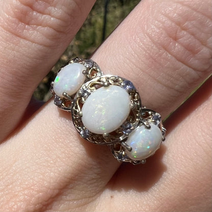 Close-up of a past-present-future three-stone Australian opal ring in sterling silver with violet tanzanite accents, worn on a hand in natural light.
