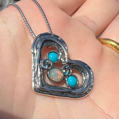 A sterling silver heart necklace set with opal, turquoise, and blue topaz shown close-up in sunlight at an angle.