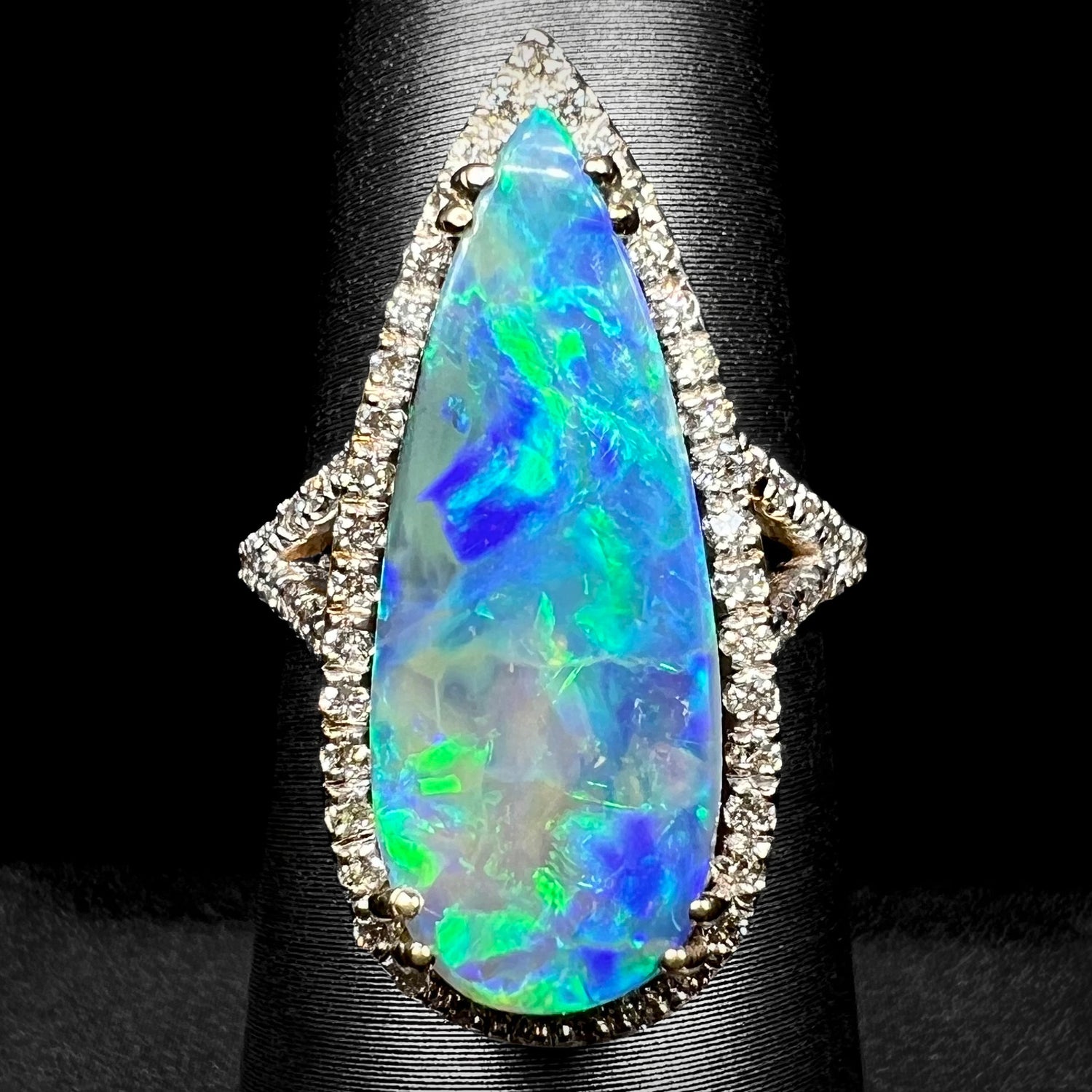 Front view of a large, pear shaped boulder opal engagement ring with a VS2 diamond halo, shown on a ring display against black background.