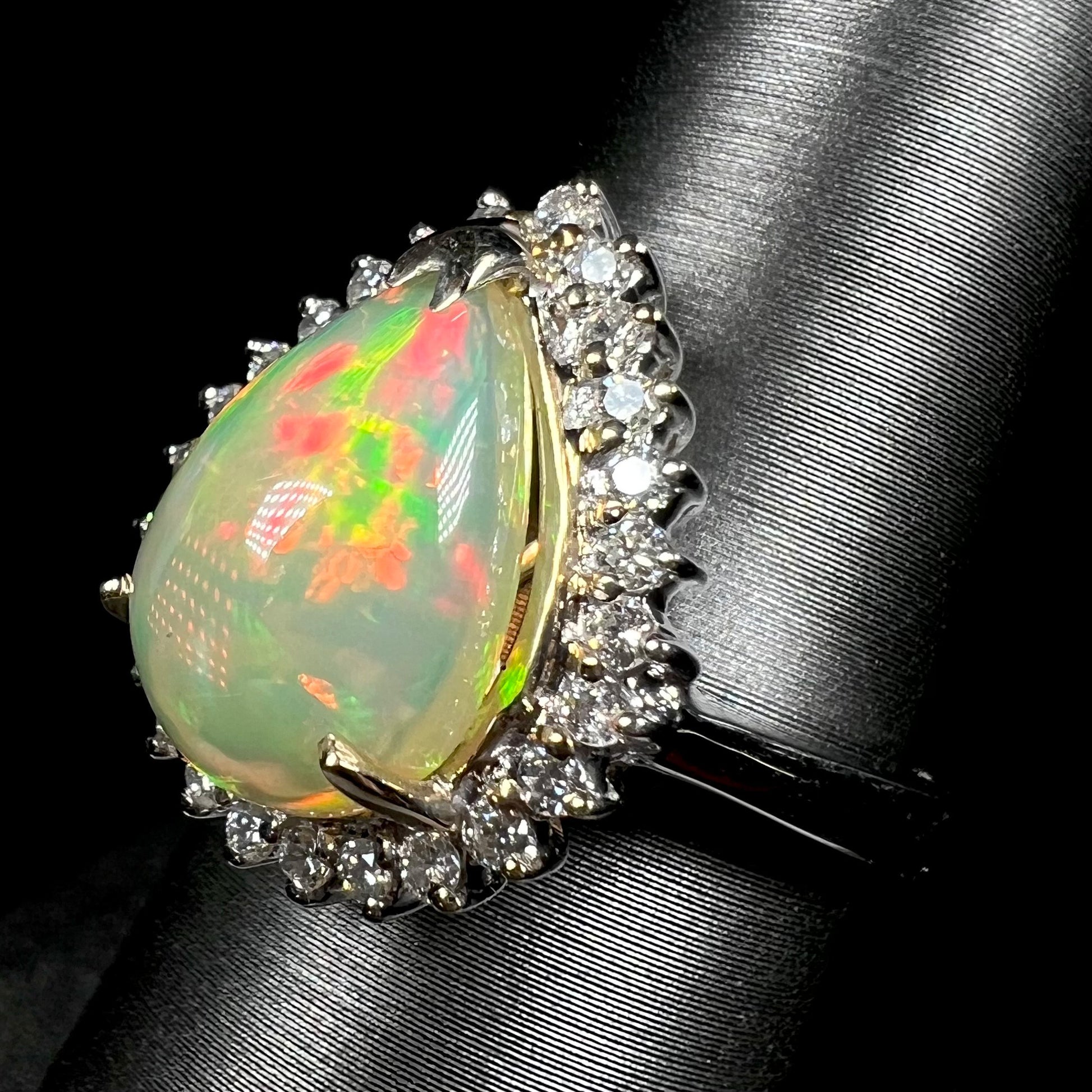 Angled macro view of pear cut Ethiopian opal and diamond halo ring in white gold.  The opal has red and green play of color.