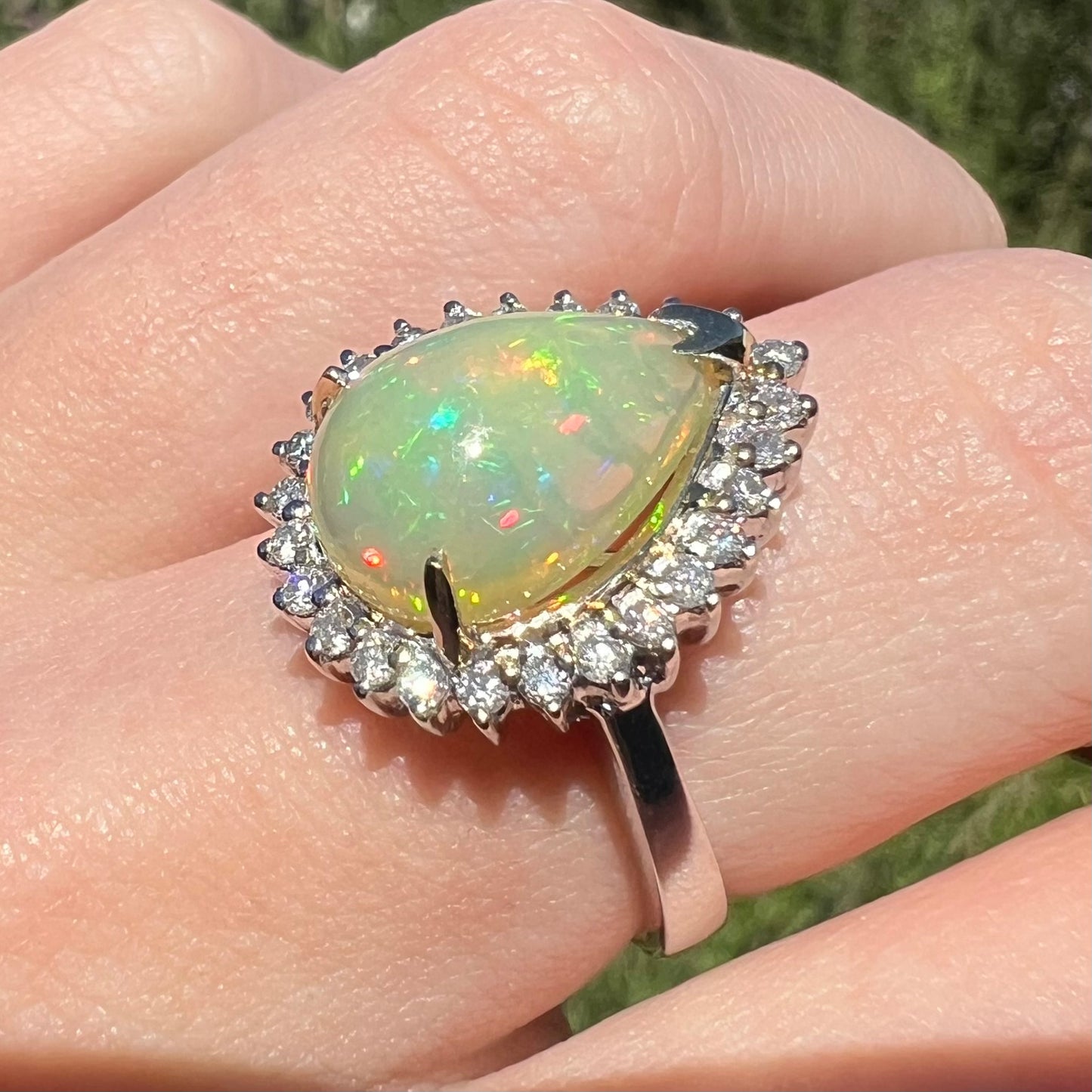 Pear cut Ethiopian opal engagement ring with diamond halo in 18k white gold, shown from close-up angle on finger in natural light.
