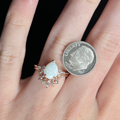 Pear cut opal and moissanite engagement and wedding ring set, worn on hand next to US dime coin for scale
