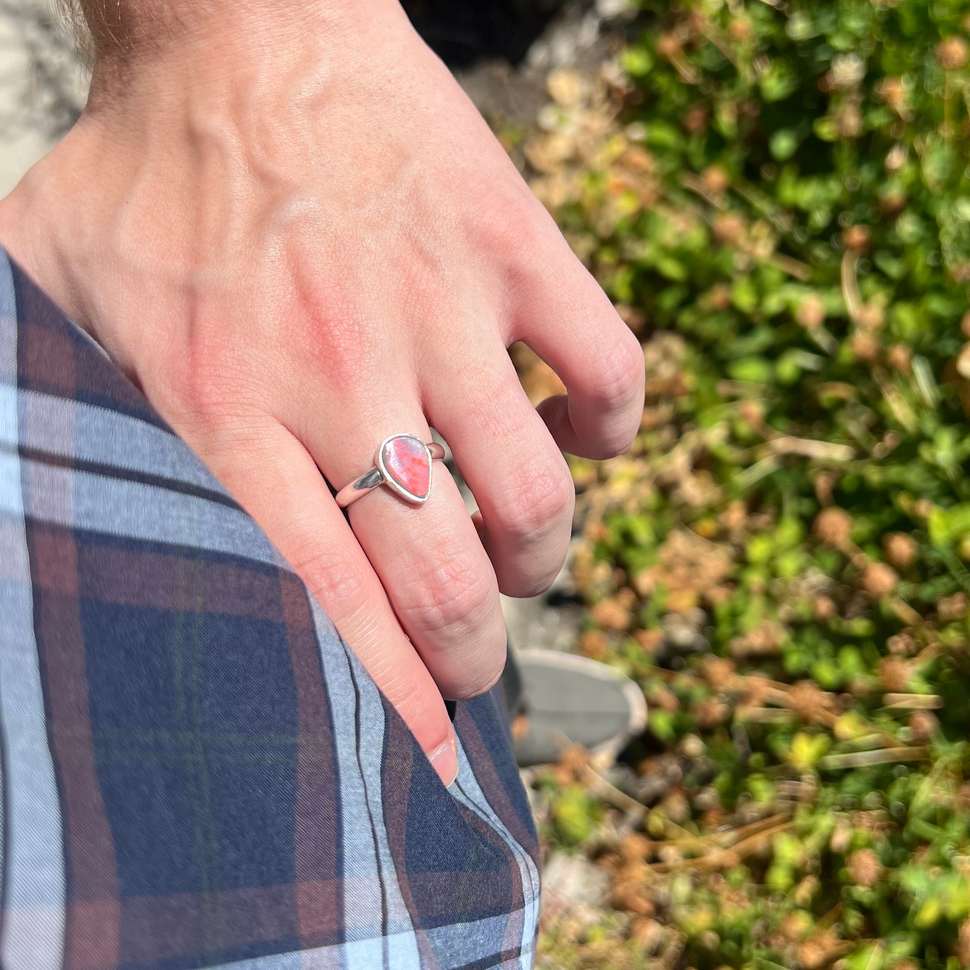 Hand resting on person's hip while wearing a sterling silver pear shaped Australian opal ring.  Sunlight shows a bright red flash of color across the opal.