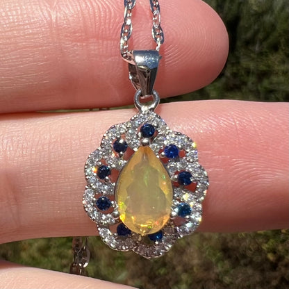 Close-up of pear shaped Ethiopian opal pendant with sparkling CZ accents, held in hand under natural light