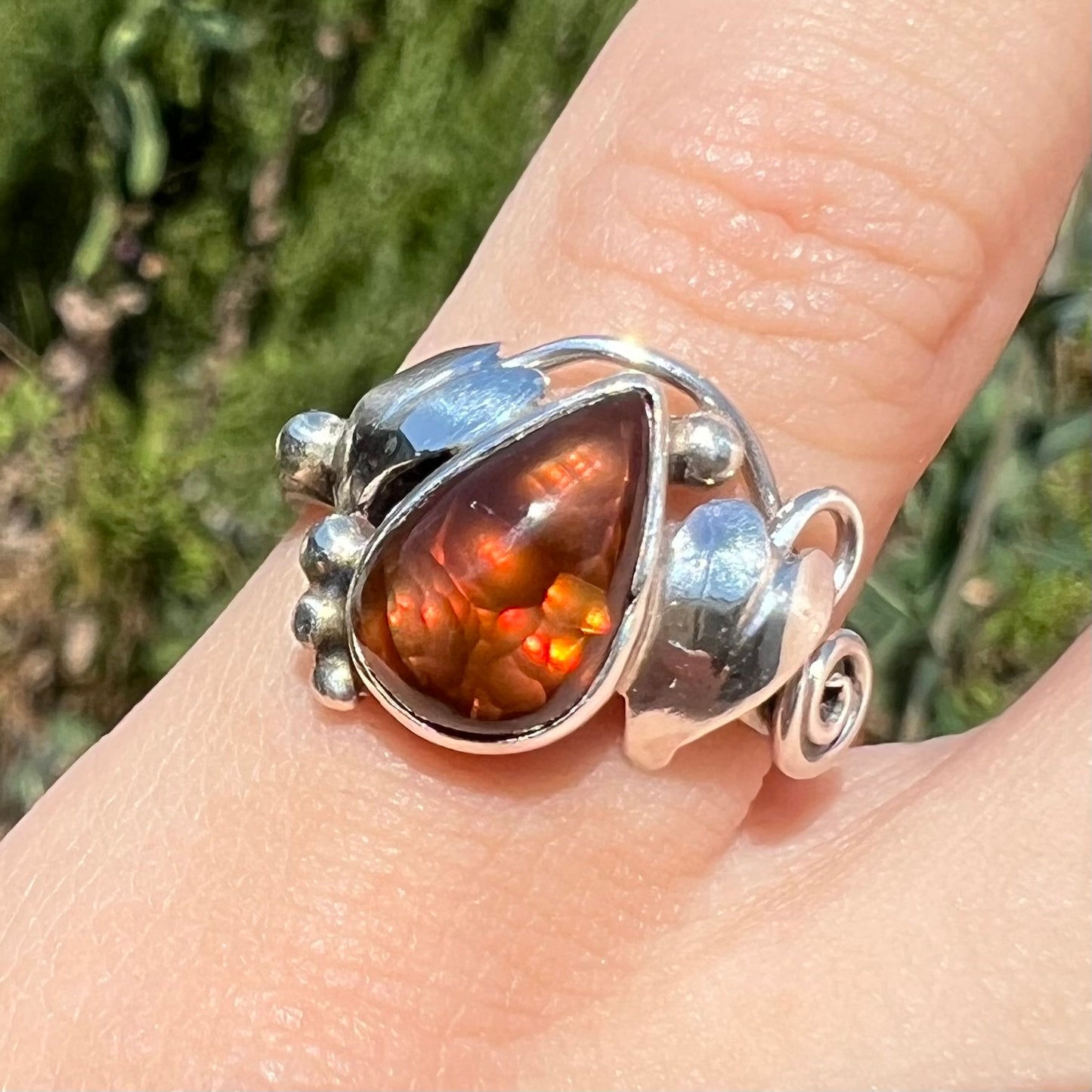Close-up front view of a ladies' pear shaped red fire agate ring with a sterling silver leaf design in sunlight.