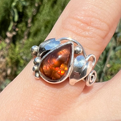 Close-up front view of a ladies' pear shaped red fire agate ring with a sterling silver leaf design in sunlight.