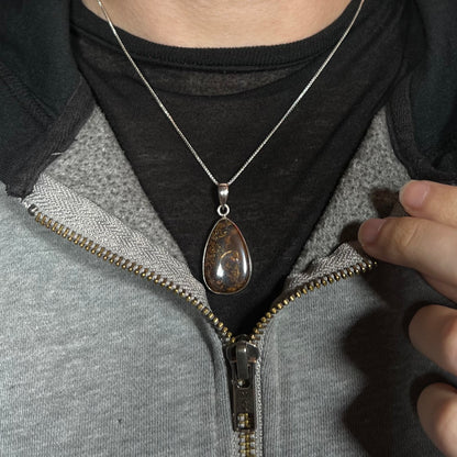 A pear shaped Koroit boulder opal pendant in sterling silver shown worn around a neck against a dark shirt.