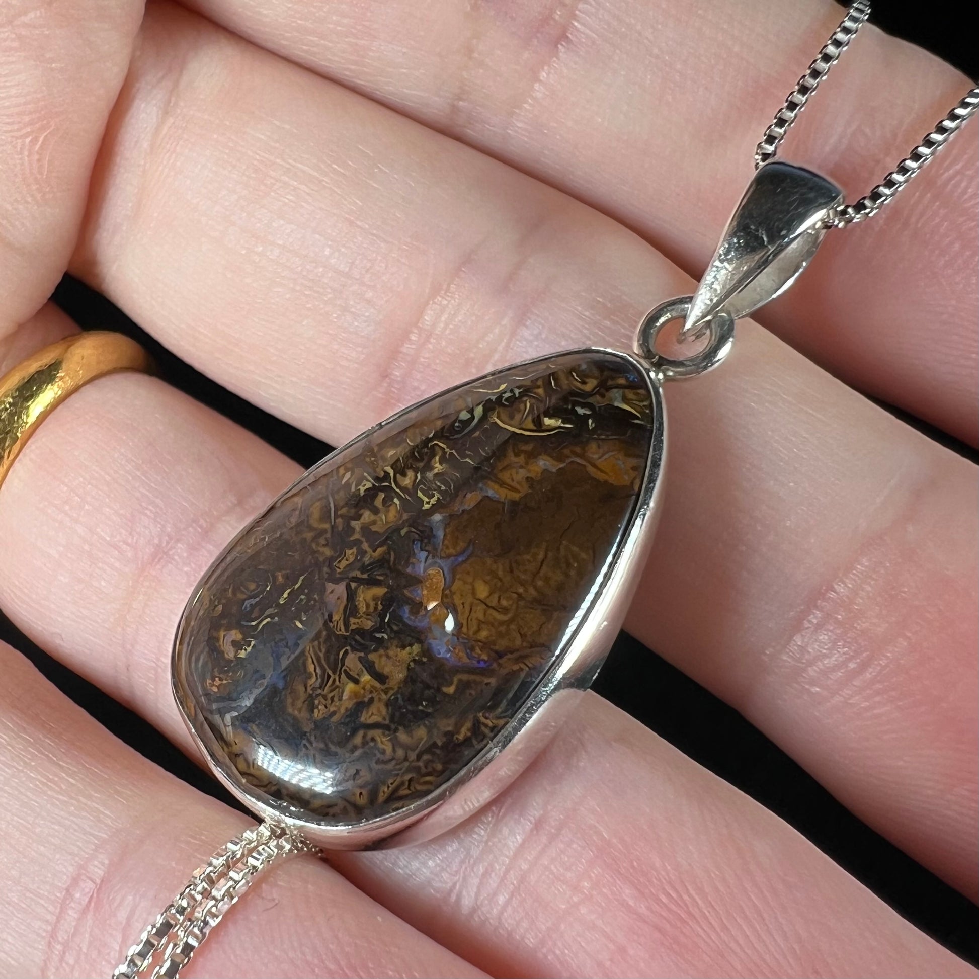 A pear shaped Koroit boulder opal pendant in sterling silver shown close-up in a hand from an angle.