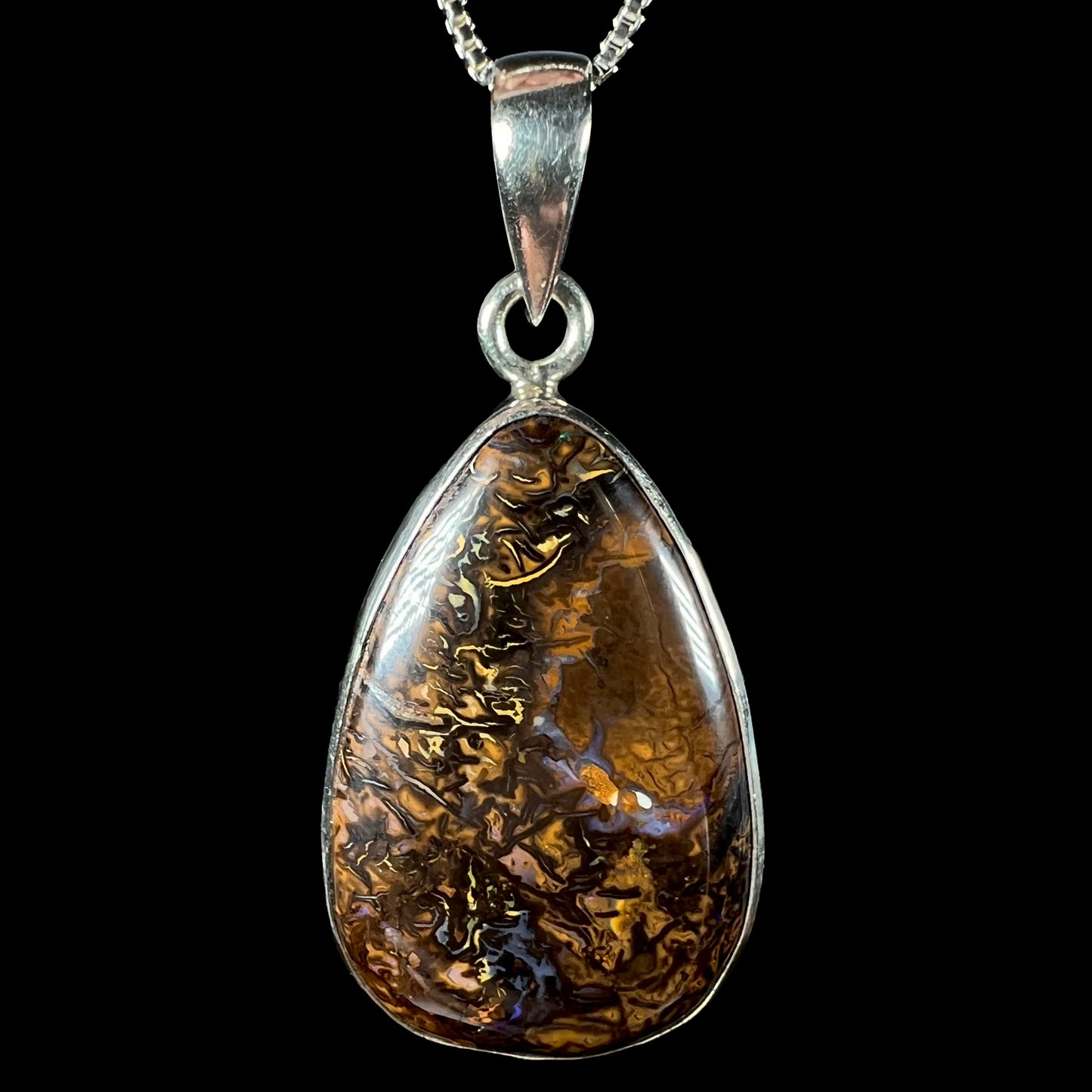 A pear shaped Koroit boulder opal pendant in sterling silver shown close-up against a black background.