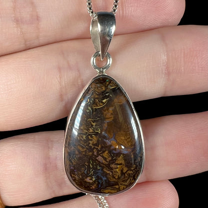 A pear shaped Koroit boulder opal pendant in sterling silver shown close-up in a hand.