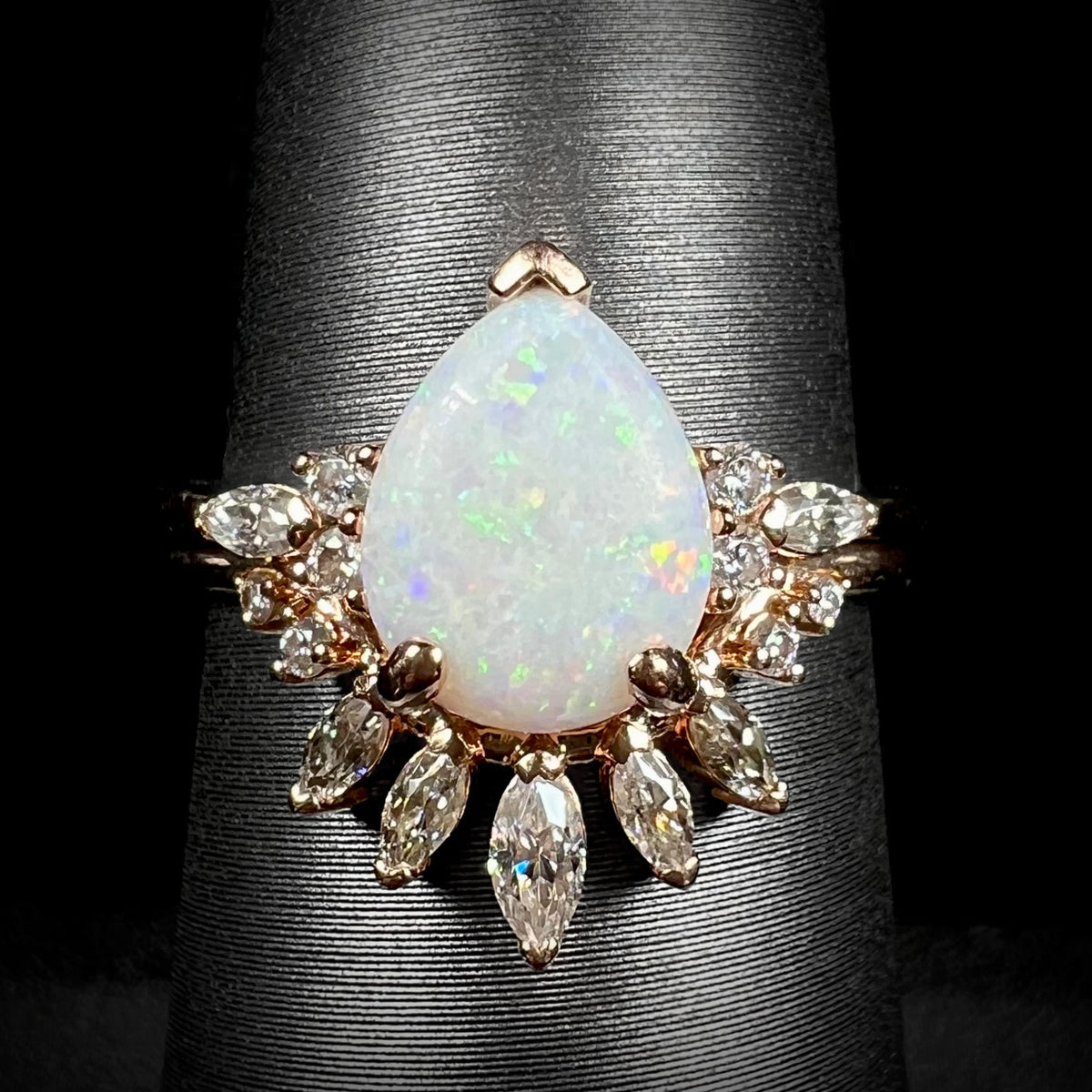 Close-up of women's pear shaped Australian opal and moissanite wedding ring set in 14k rose gold on ring display