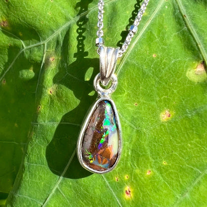 A pear shaped boulder opal necklace in sterling silver.  The opal has bright green and blue flashes.