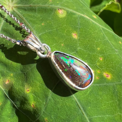 A pear shaped boulder opal necklace in sterling silver.  The opal has bright green and blue flashes.
