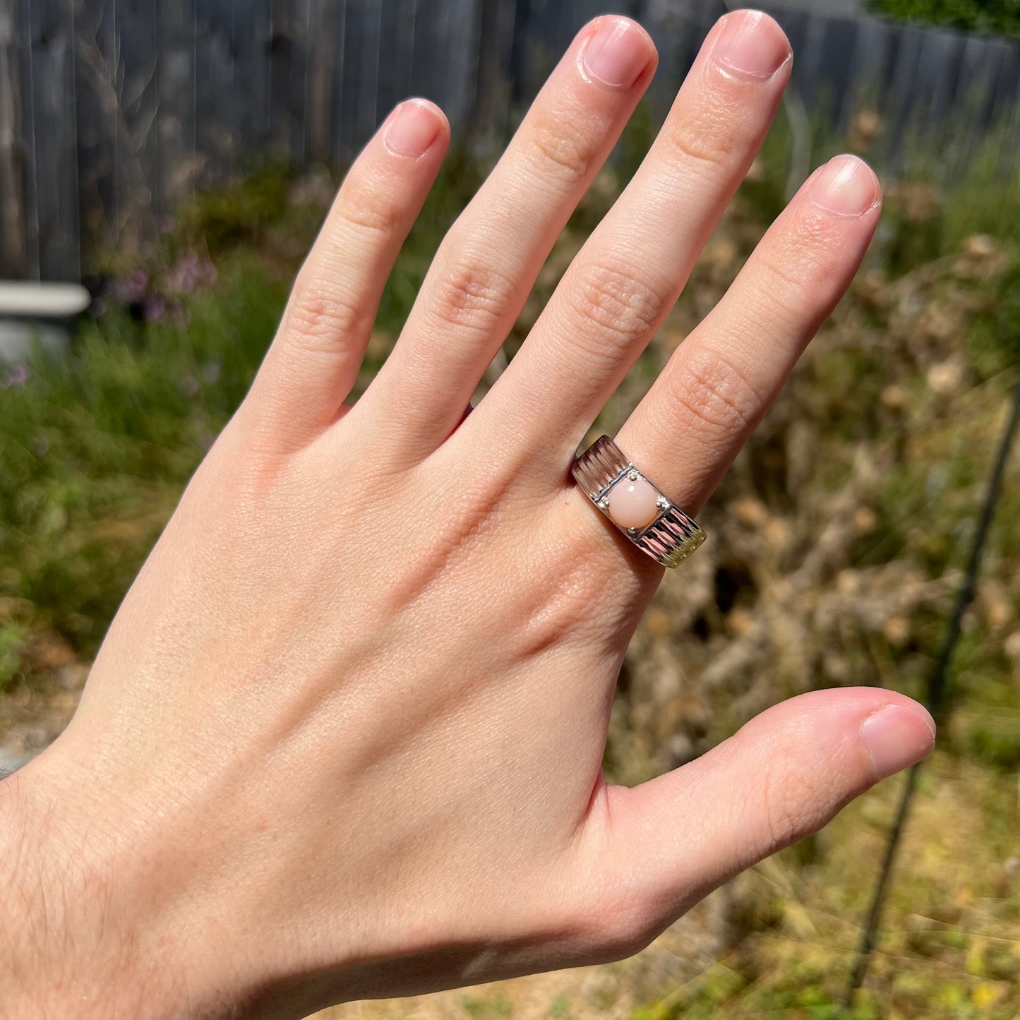 Hand wearing sterling silver Peruvian pink opal ring in natural sunlight