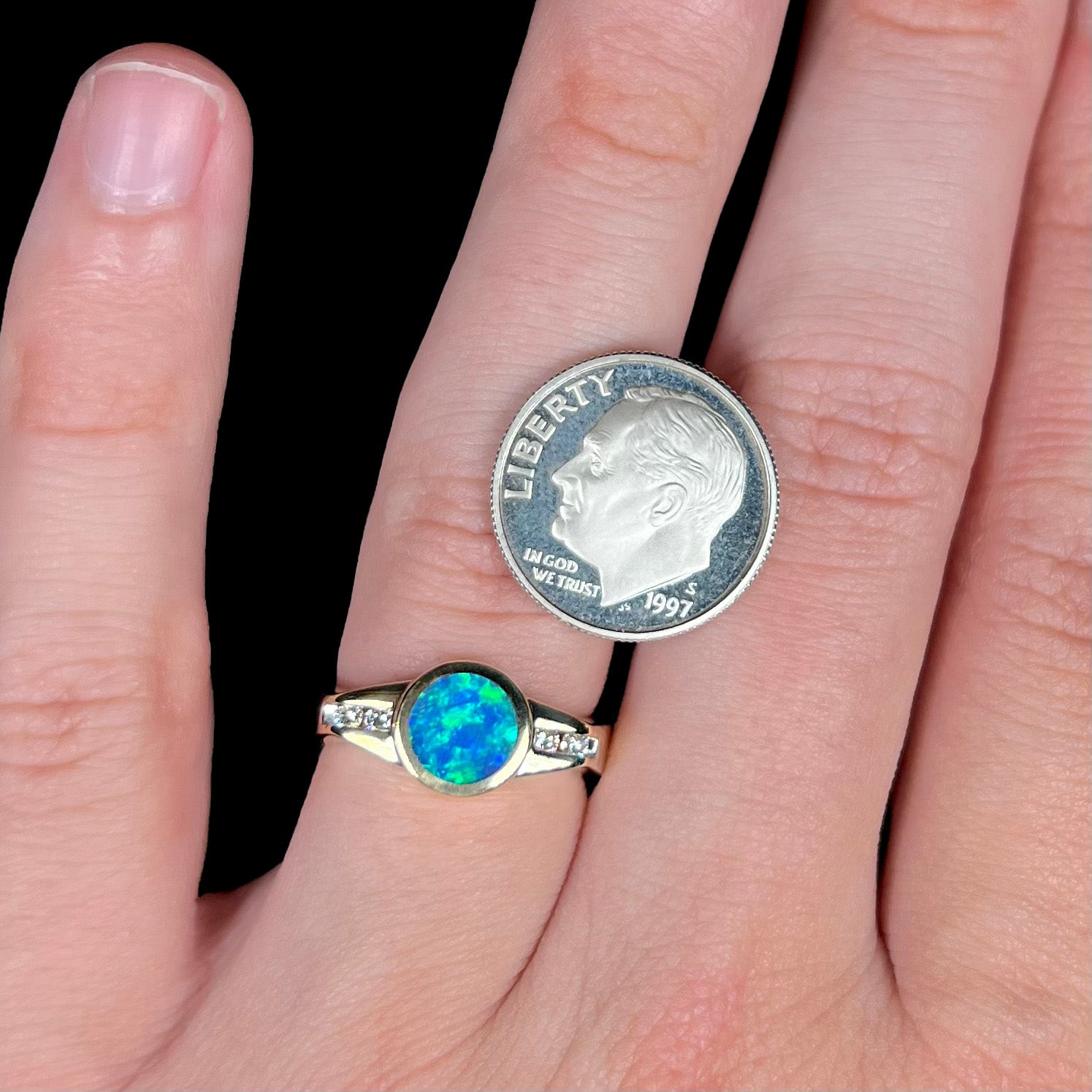 A petite unisex black boulder opal ring with green fire, worn on a finger next to a dime coin for scale.