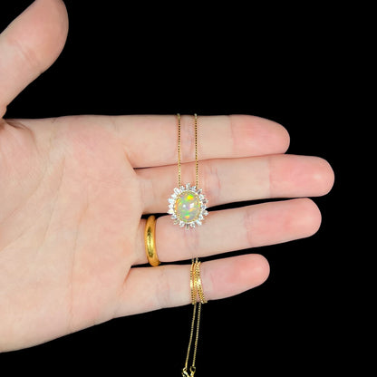 Hand holding a petite yellow gold Ethiopian opal and spiky white sapphire halo necklace on box chain.