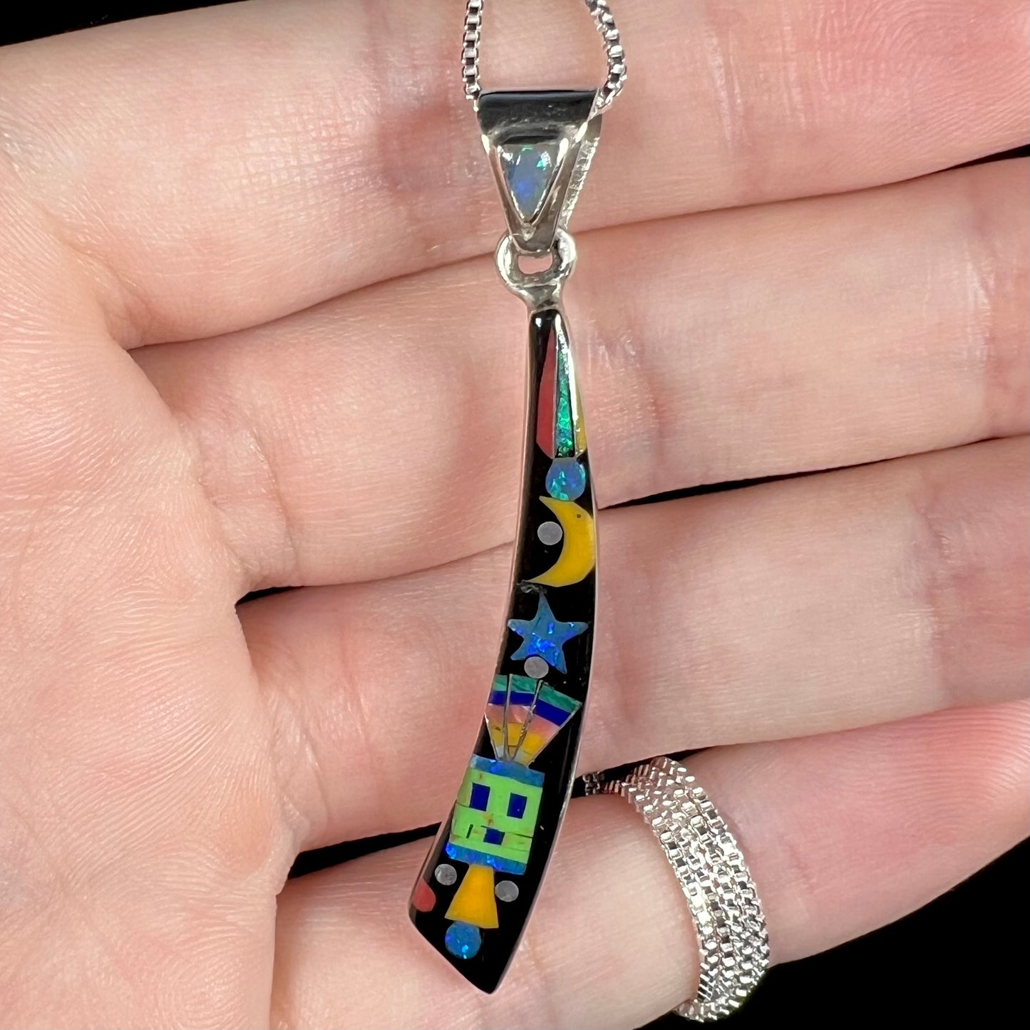 Colorful Philippines-made Southwest-style inlay pendant with star, moon, and kachina design held in a hand, shown close-up.