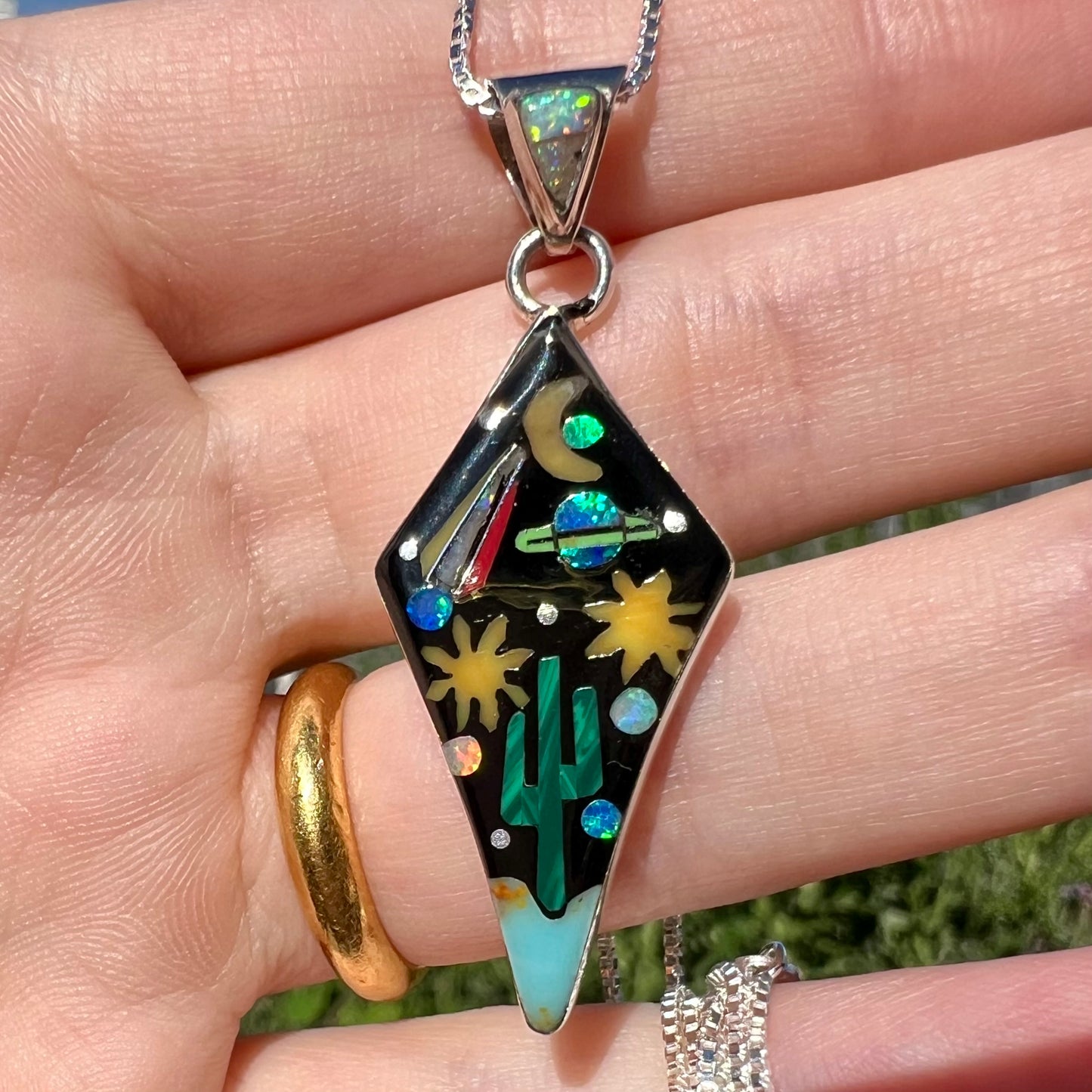 Close-up of Philippines-made silver gemstone inlay pendant with space design held in hand under natural light.