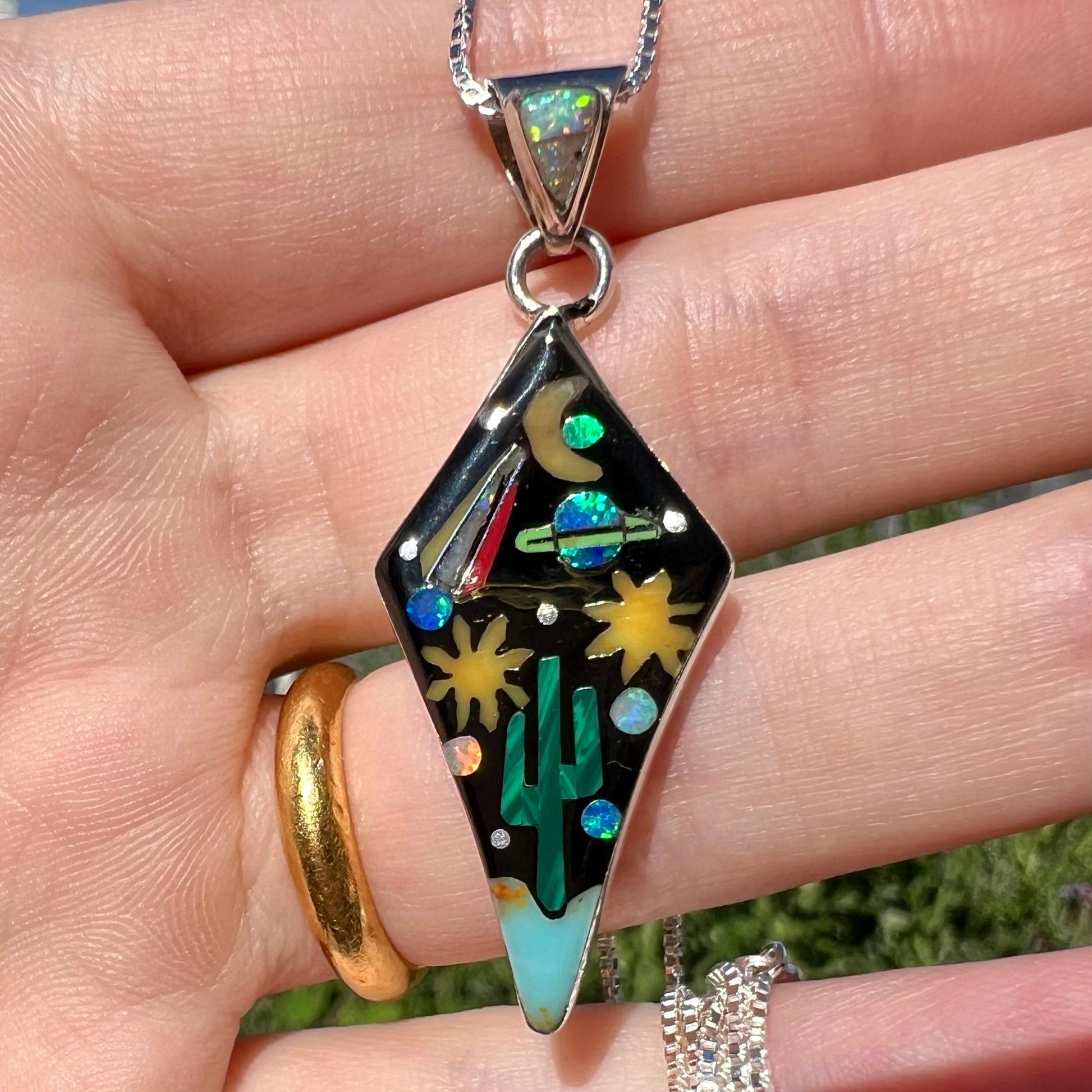 Close-up of Philippines-made silver gemstone inlay pendant with space design held in hand under natural light.