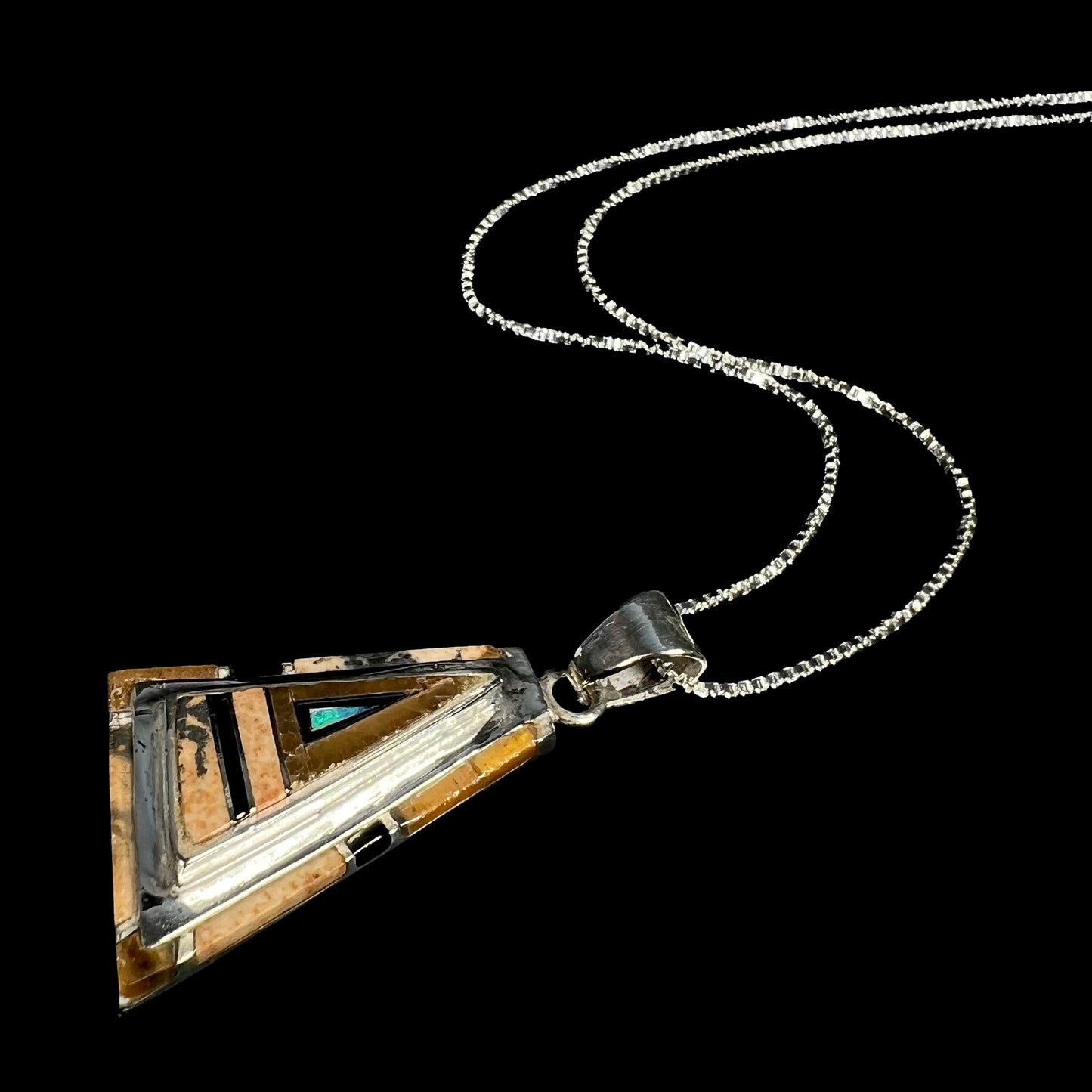 A ssilver opal, picture jasper, and onyx inlay necklace, shown from an angle laying on a black backdrop.
