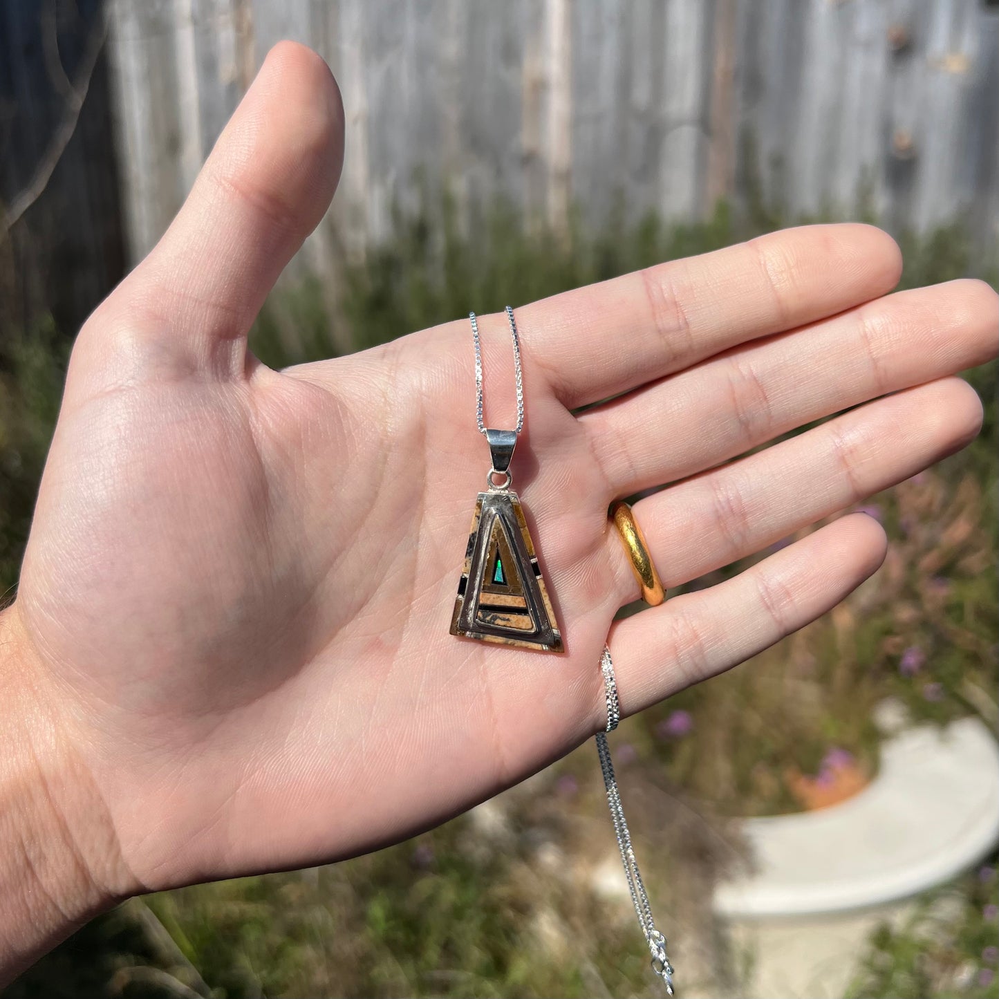 A sterling silver Australian opal, picture jasper, and onyx inlay pendant shown in a hand in sunlight.