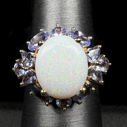 Macro view of 14k gold Australian white opal ring with cluster of tanzanite accents on ring display; the opal has green pinfire pattern