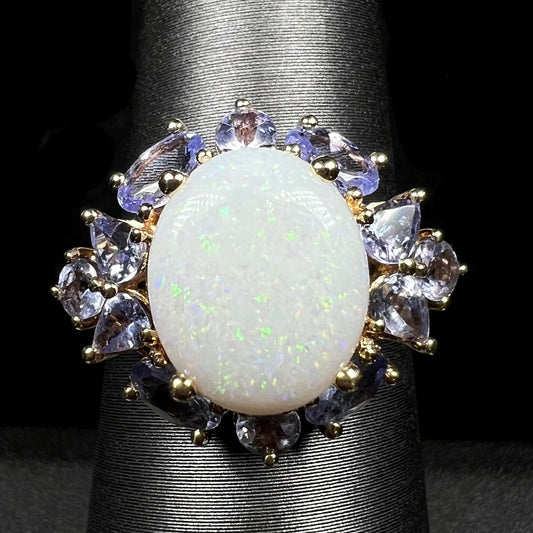 Macro view of 14k gold Australian white opal ring with cluster of tanzanite accents on ring display; the opal has green pinfire pattern