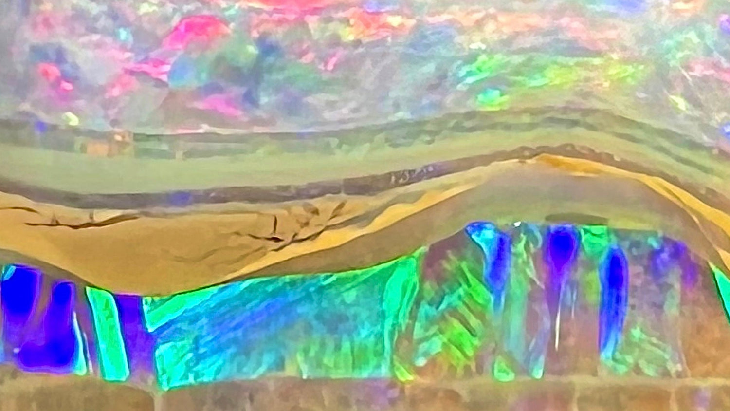 Close-up view of an Australian boulder opal.  Half of the opal is green and blue, and the other half is pink, separated by an ironstone partition.