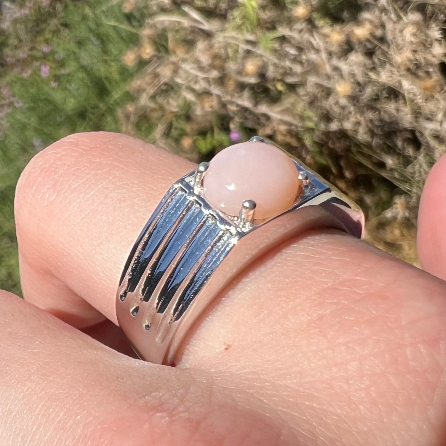 Pink common opal ring in sterling silver worn on finger under natural sunlight