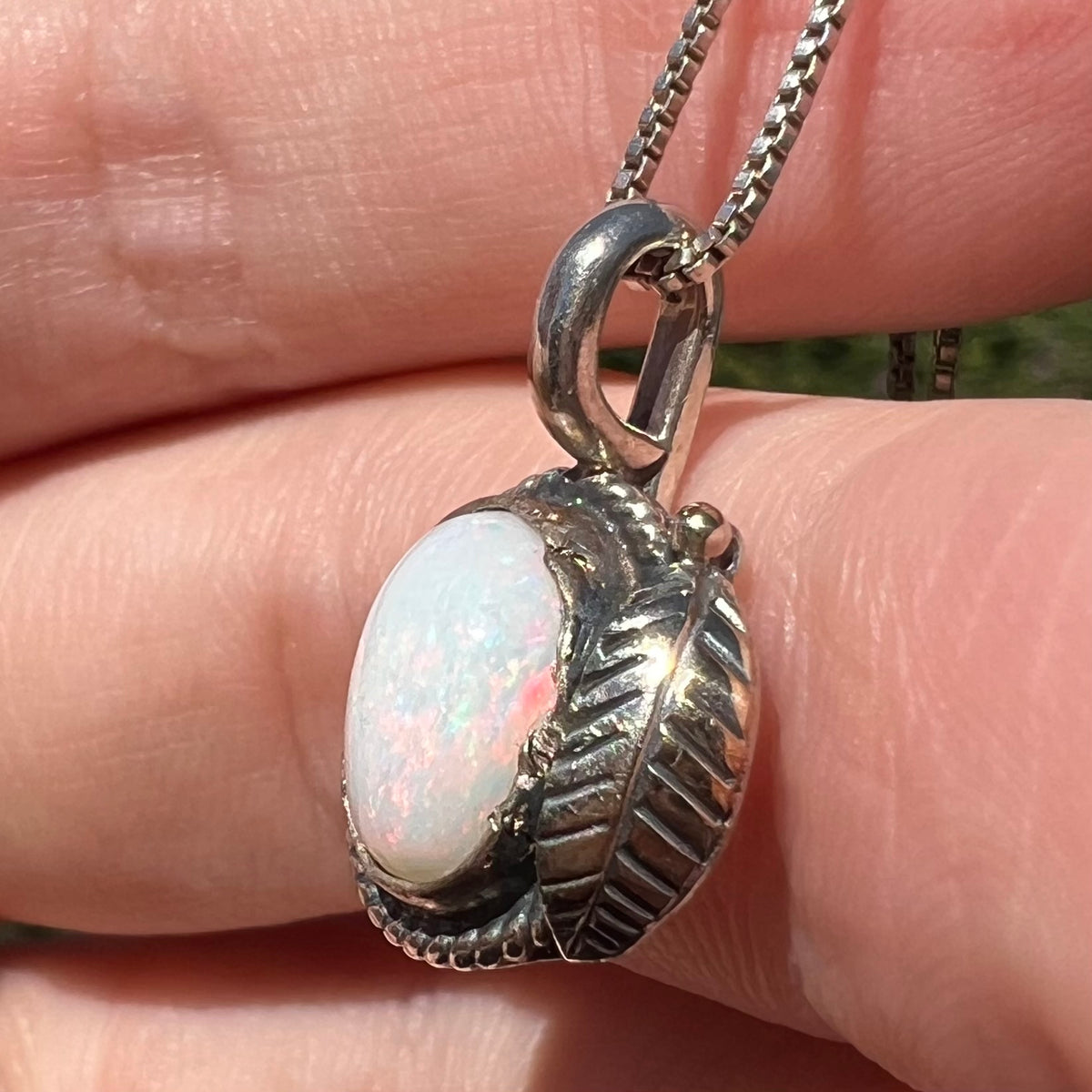 Pink flashes seen from side view of sterling silver Coober Pedy, Australian opal pendant with American Southwest style feather design, held in hand under sunlight