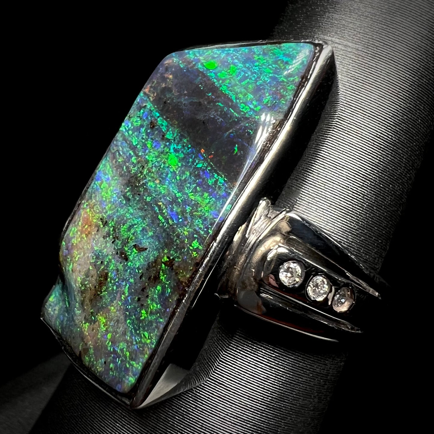 A platinum Australian boulder opal and diamond ring, shown at an angle on a ring display.  The opal has green color play.