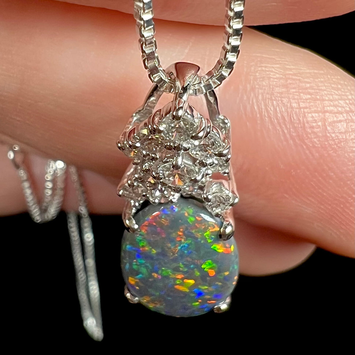 Top-down close-up view of a platinum black opal pendant with a crown of diamond accents.  Multicolor green, blue, red, and orange play-of-color seen in opal.