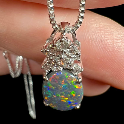 Top-down close-up view of a platinum black opal pendant with a crown of diamond accents.  Multicolor green, blue, red, and orange play-of-color seen in opal.