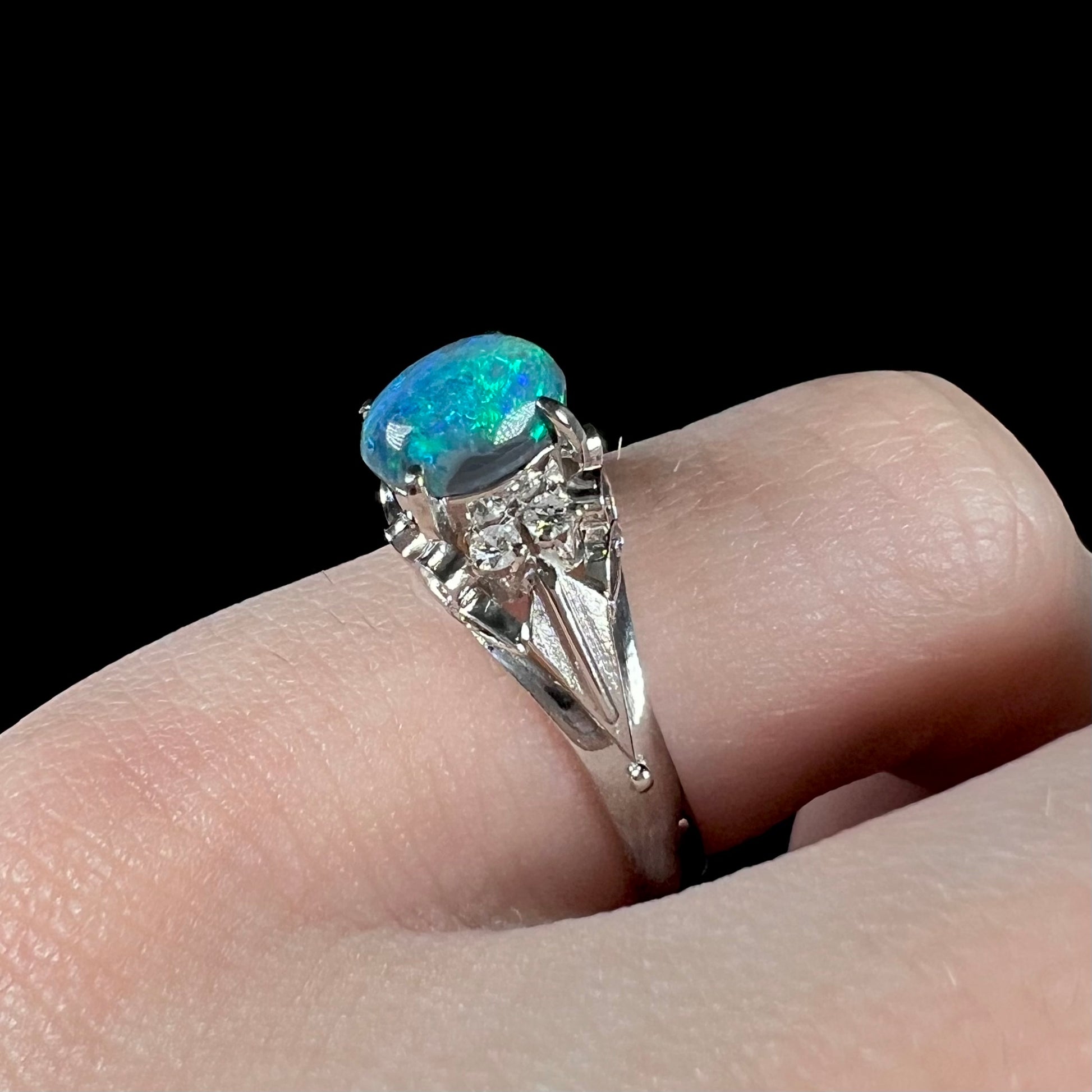 A 0.89ct Lightning Ridge black opal engagement ring set in platinum with diamond accents on a finger.